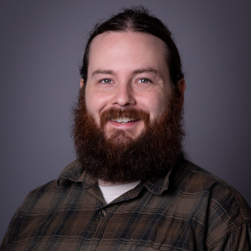 headshot photo of Ben Gladstone wearing a plaid shirt on a gray backdrop
